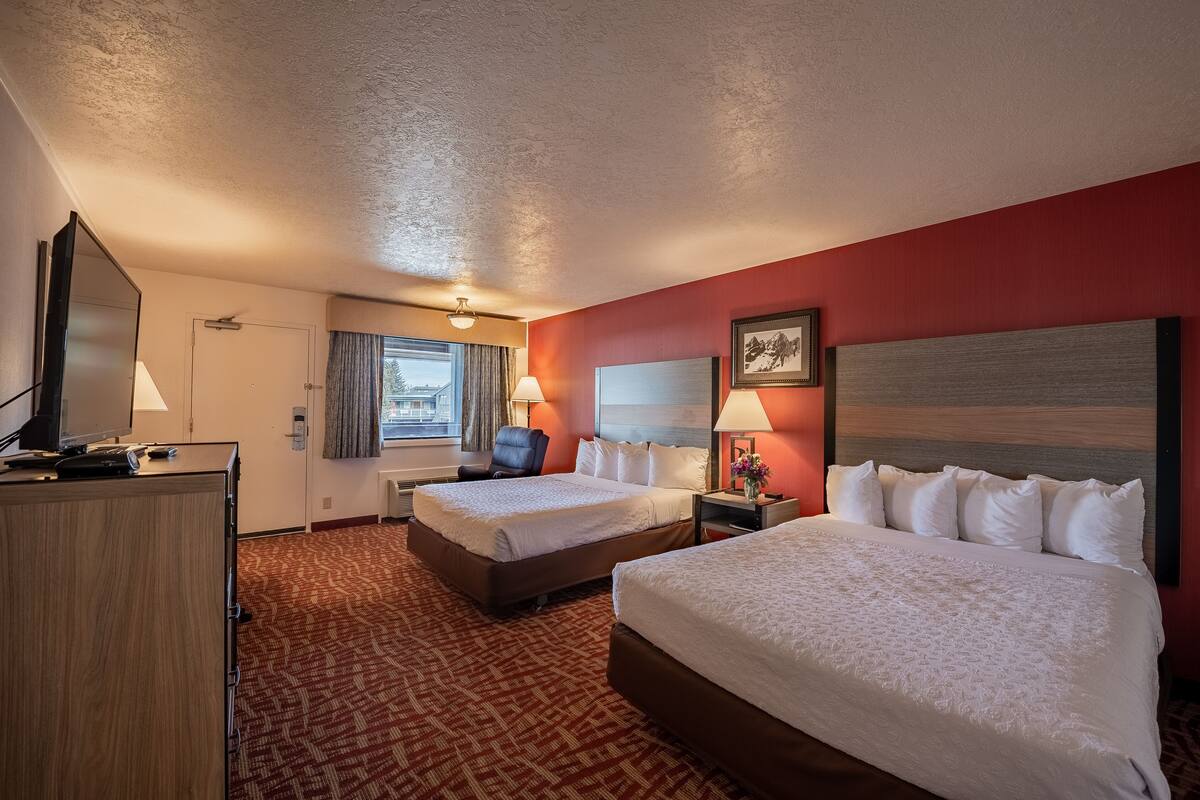A hotel room with two beds, a desk with a TV, a chair, and a window with curtains.