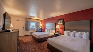 A hotel room with two beds, a desk with a TV, a chair, and a window with curtains.