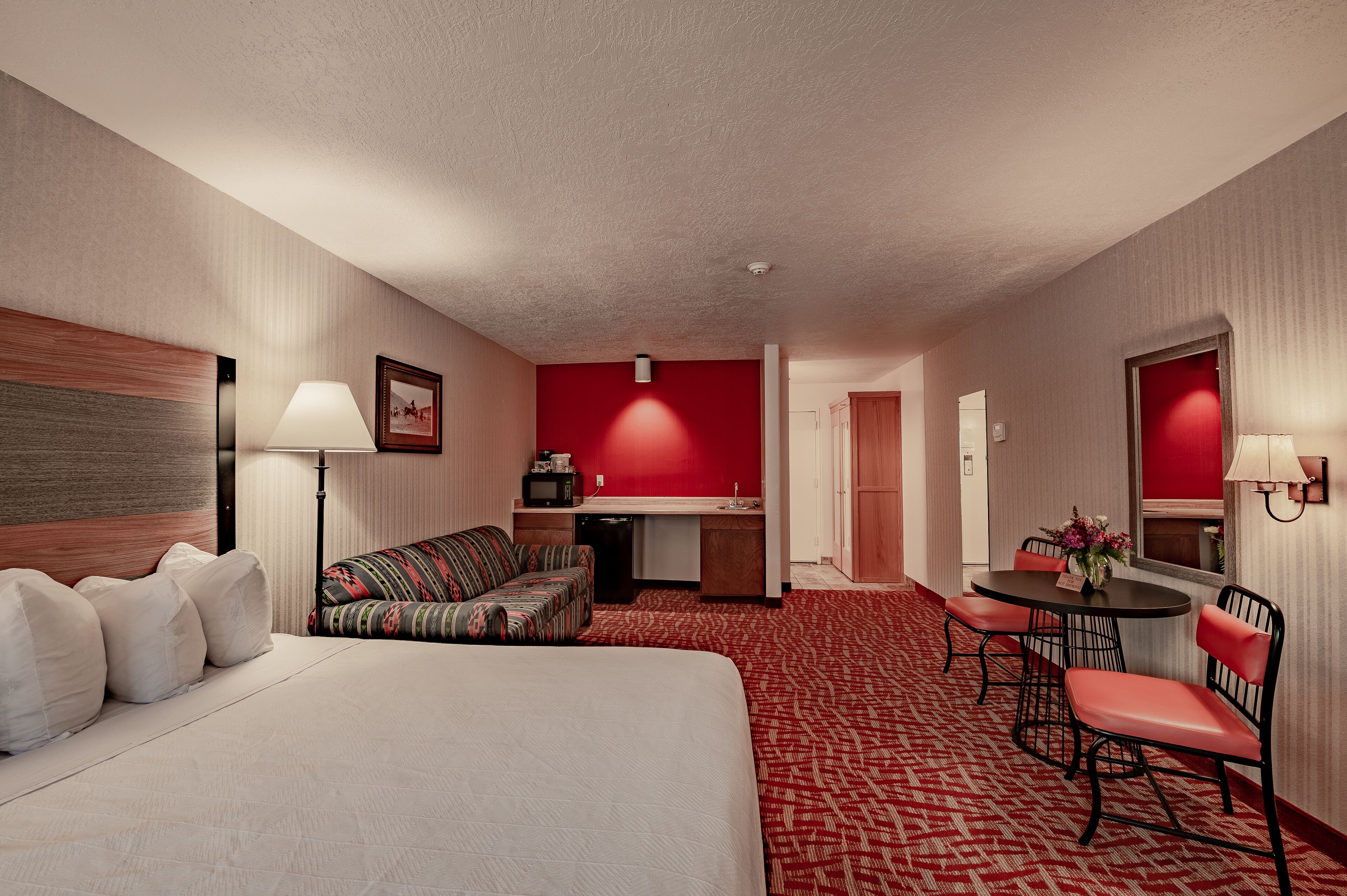A hotel room with a bed, a sofa, a desk, a dining table with chairs, and a kitchenette.