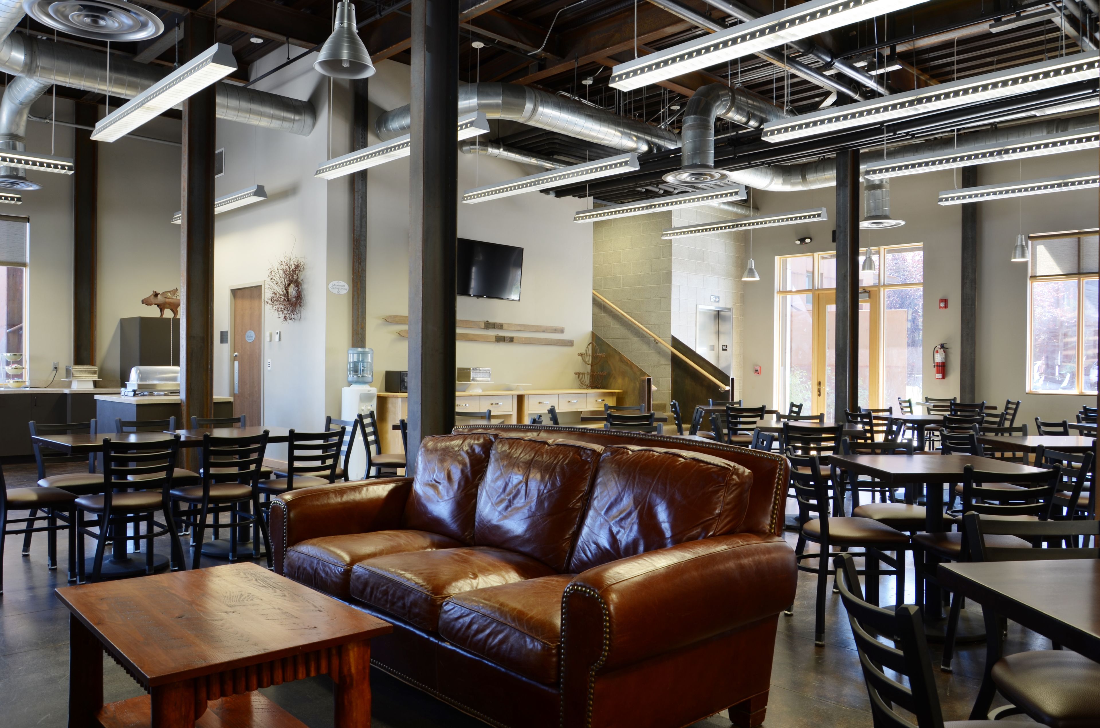 A spacious indoor area with multiple tables and chairs, a large brown leather couch, and a staircase leading to an upper level.