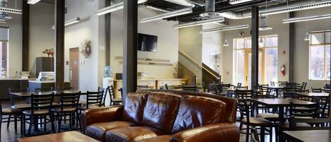 A spacious indoor area with multiple tables and chairs, a large brown leather couch, and a staircase leading to an upper level.