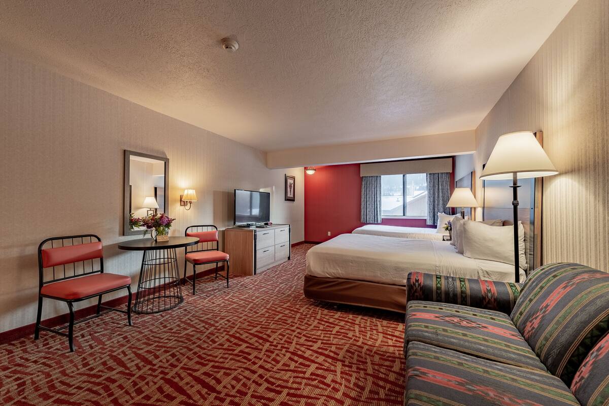 A hotel room with a bed, a sofa, a desk with a chair, a television, and a window with curtains.