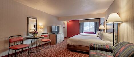 A hotel room with a bed, a sofa, a desk with a chair, a television, and a window with curtains.