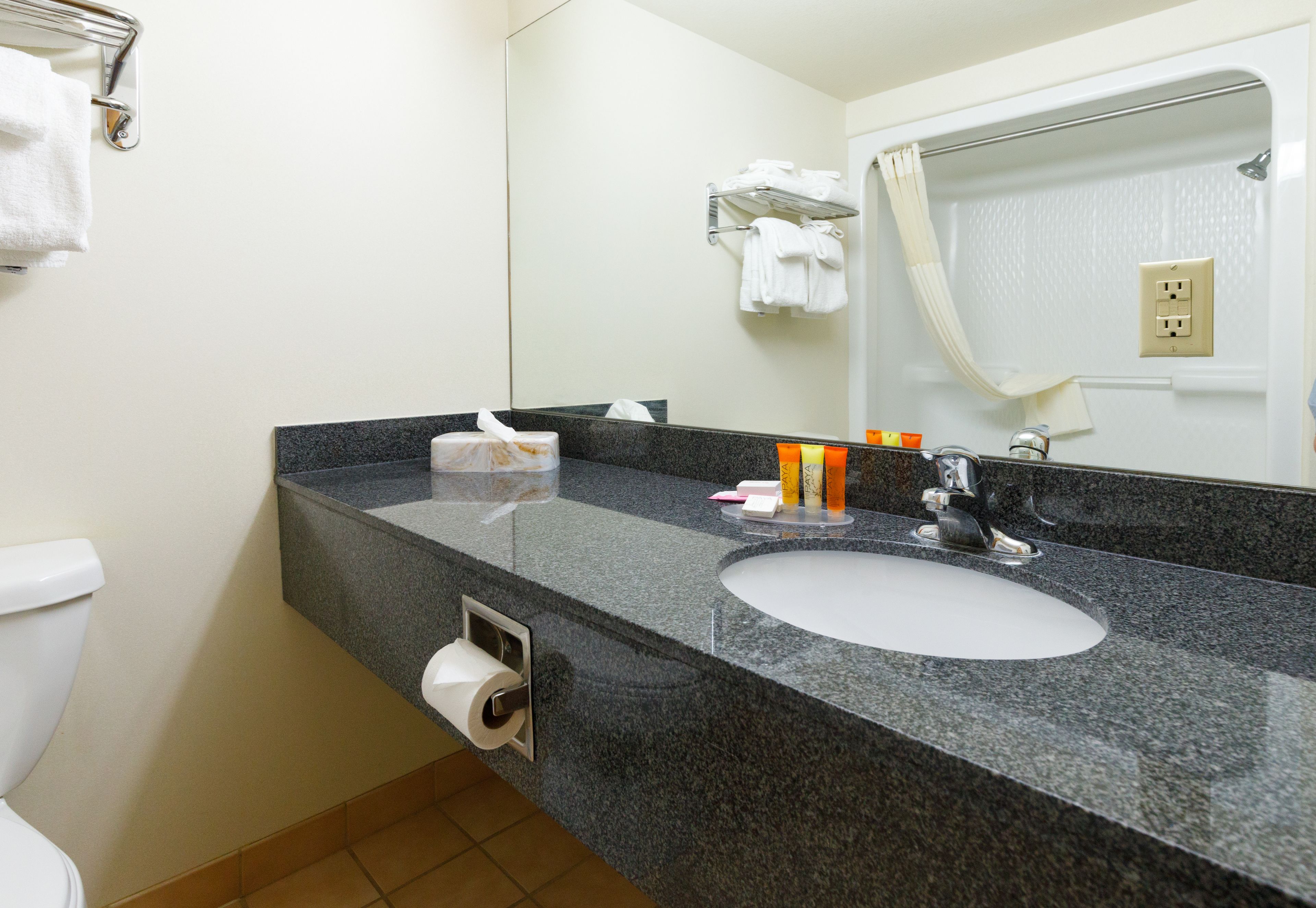 A bathroom with a granite countertop, a white sink, a mirror, and a towel rack.