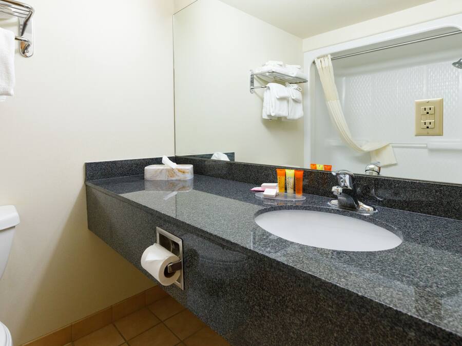 A bathroom with a granite countertop, a white sink, a mirror, and a towel rack.