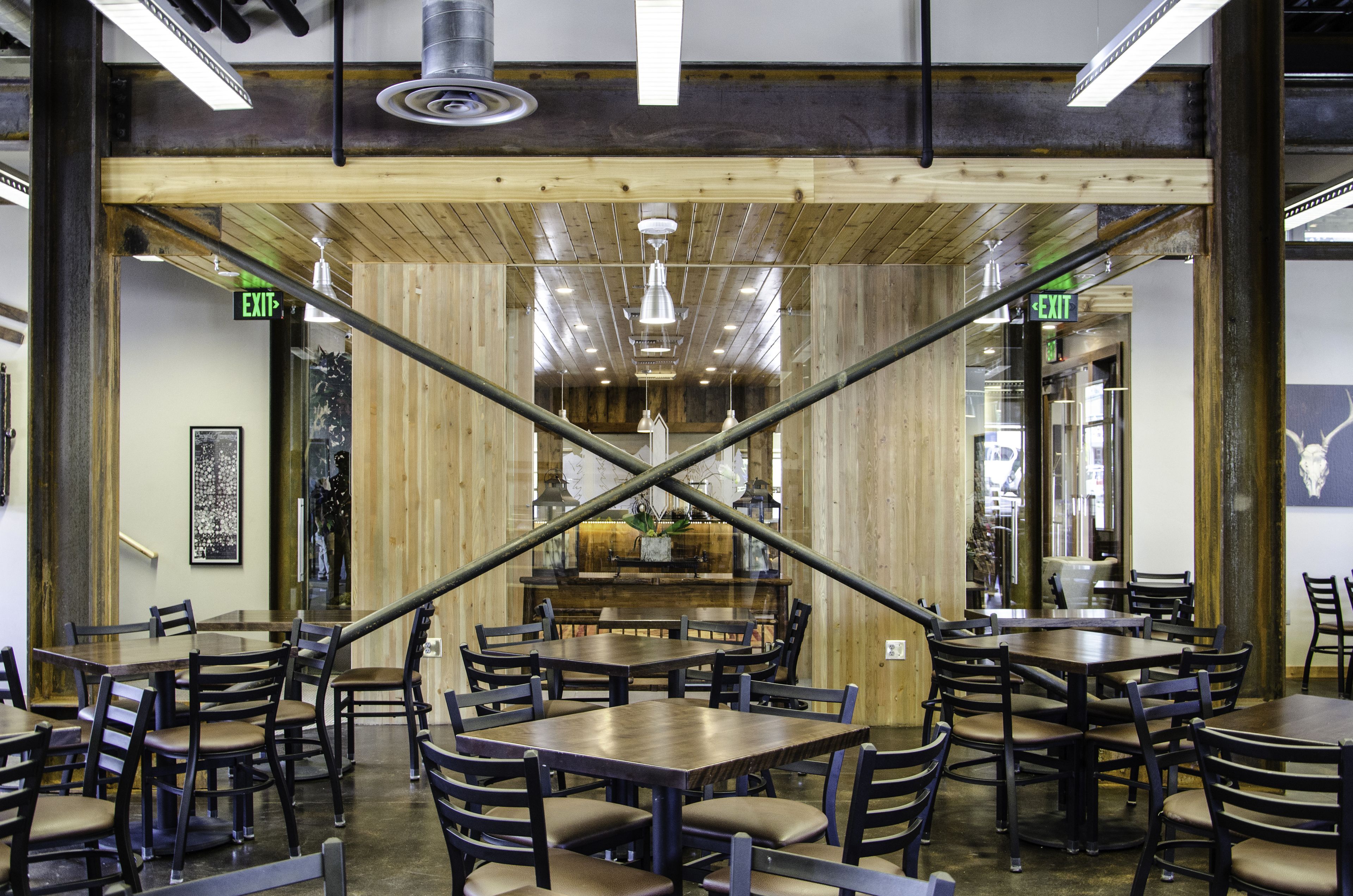 Interior de restaurante con paredes de madera, varias mesas y sillas, y señalización de salida visible.