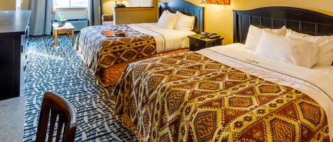 A hotel room with two beds, a desk, a chair, and a window with curtains.