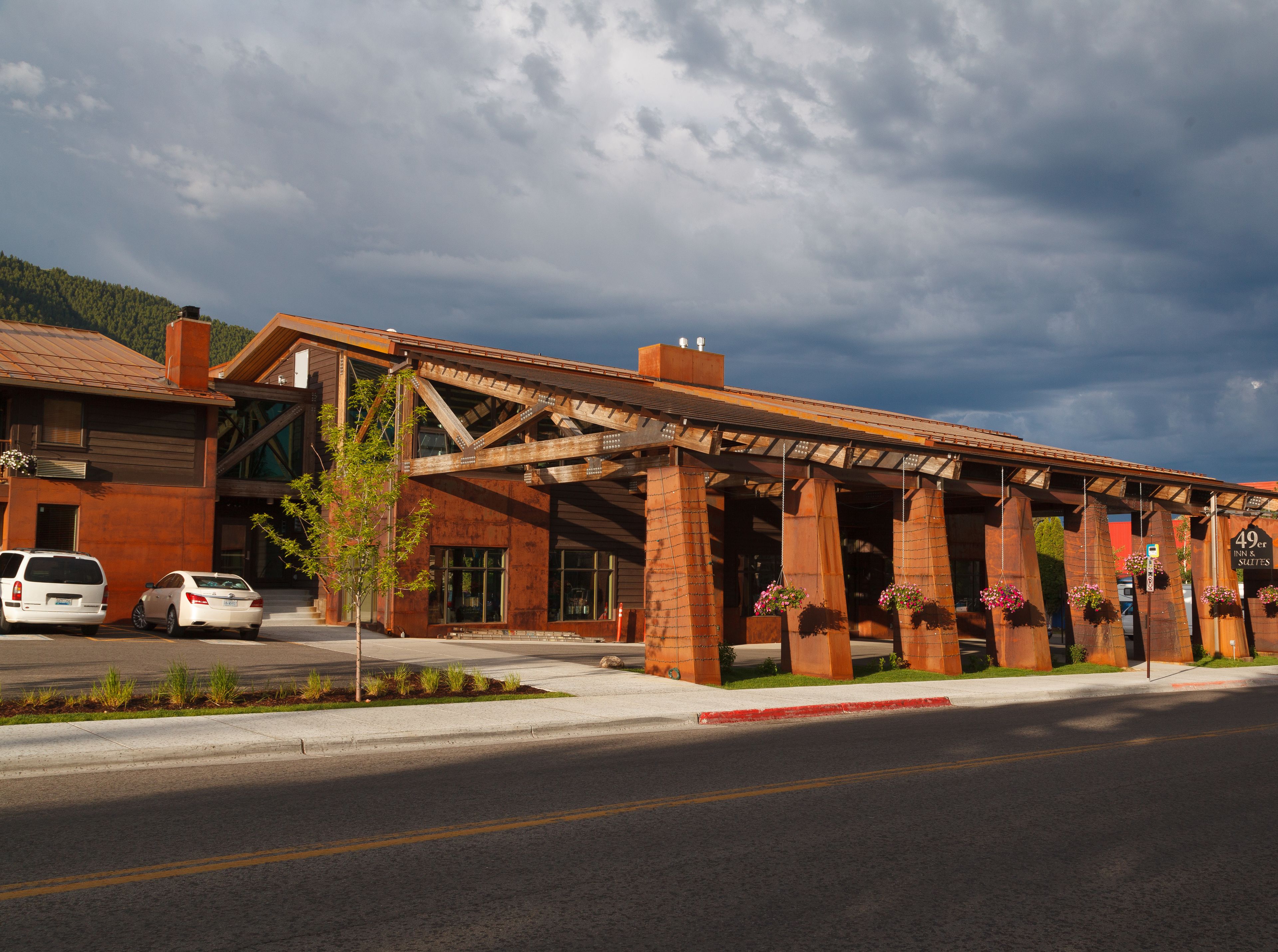 A hotel with a rustic exterior, a covered outdoor area with hanging flower baskets, and a clear sky.
