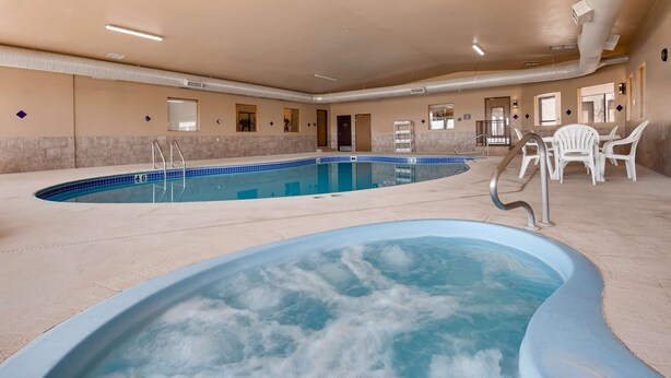 A large indoor swimming pool with a hot tub area, surrounded by beige walls and a tiled floor.