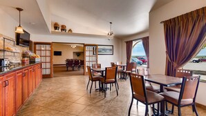 A hotel dining area with wooden furniture, a buffet counter, and a view of parked cars outside.