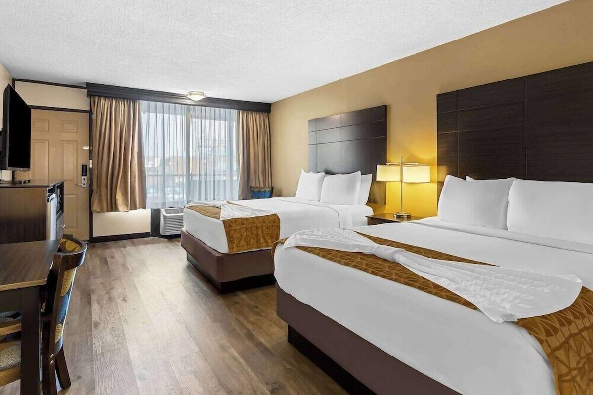 A hotel room with two beds, a desk, a chair, a TV, and a window with curtains.