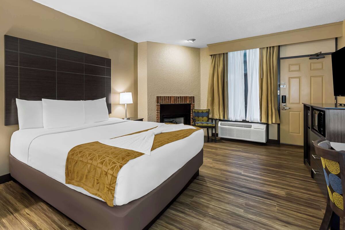 A hotel room with a large bed, a TV, a fireplace, and a desk with a chair.