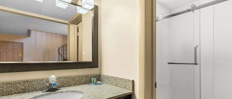 Un baño con lavamanos de encimera de granito, espejo y cabina de ducha de vidrio.