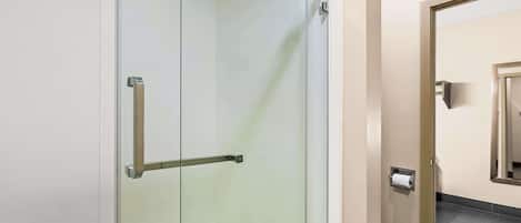 A glass-enclosed shower stall with a towel rack and a toilet paper dispenser.