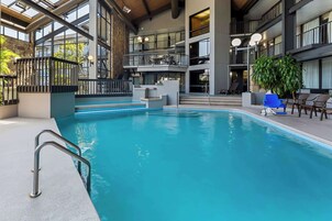 An indoor swimming pool with a metal ladder, a staircase, and a seating area with chairs and a potted plant.