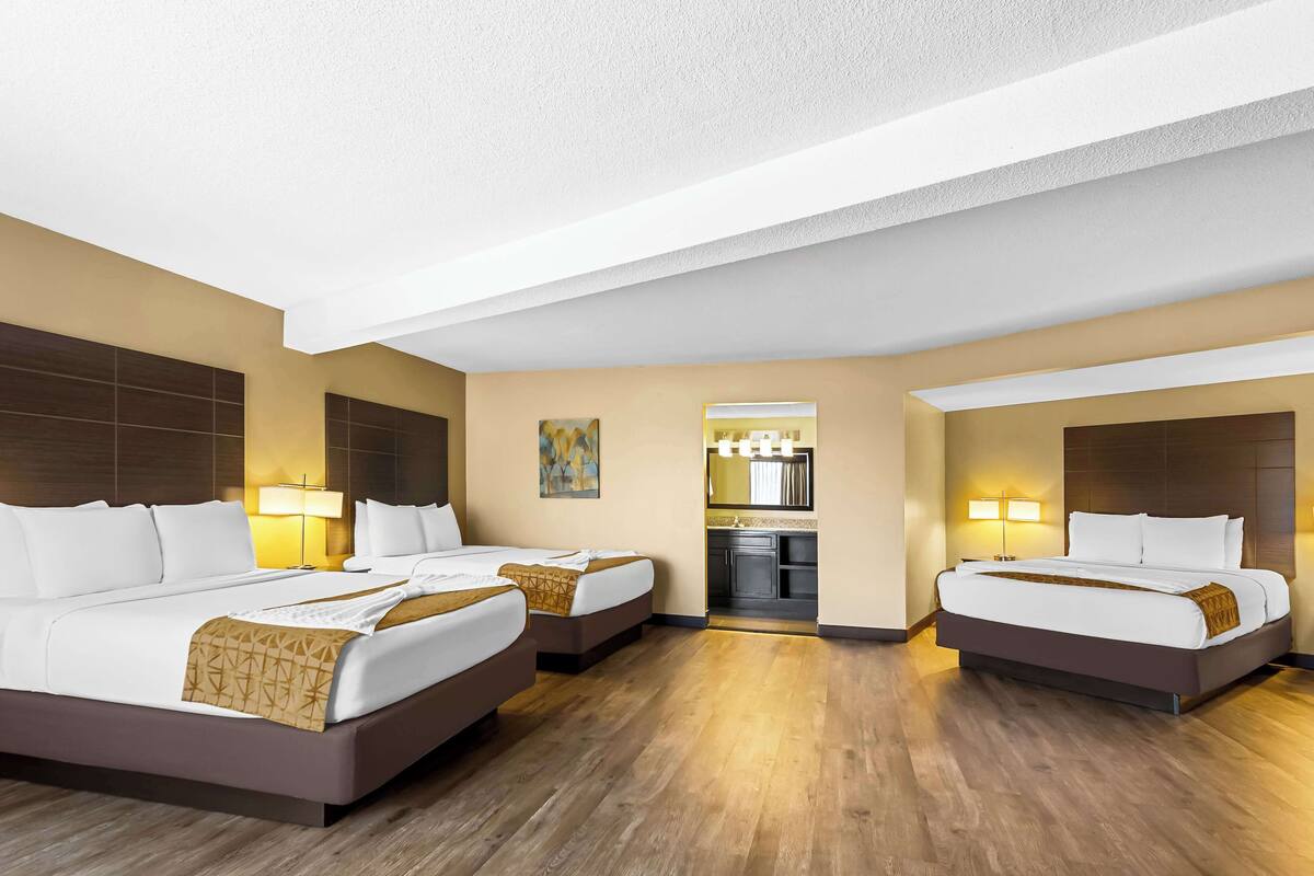 A hotel room with two beds, a kitchenette, and a bathroom.