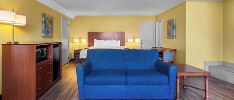 Una habitación de hotel con un sofá azul, un armario de madera, una cama con ropa blanca y dos lámparas de pared.