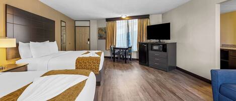A hotel room with two beds, a desk, a television, and a seating area.