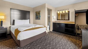 Ein Hotelzimmer mit einem großen Bett, einem Nachttisch mit Lampe, einem Badezimmer mit Spiegel und Waschbecken.