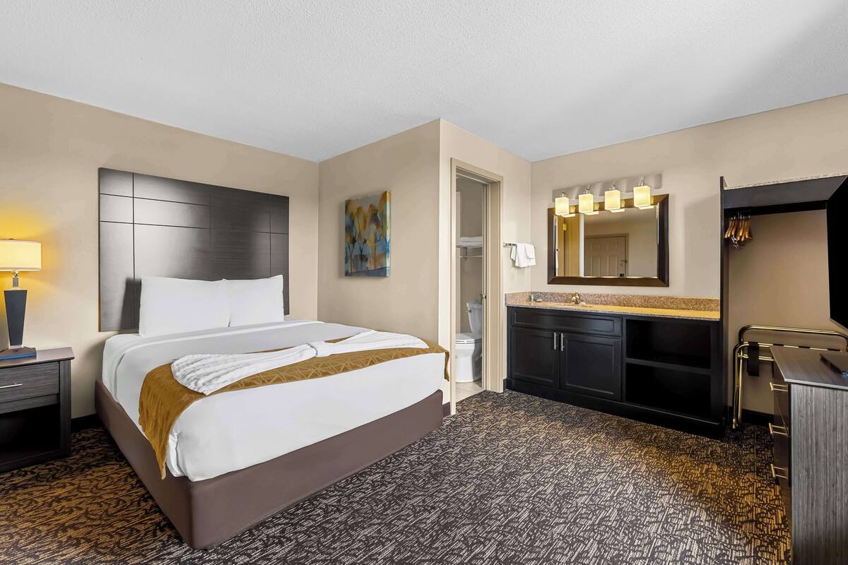 A hotel room with a large bed, a bedside table with a lamp, a bathroom with a mirror, and a sink.