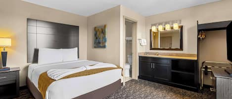 A hotel room with a large bed, a bedside table with a lamp, a bathroom with a mirror, and a sink.