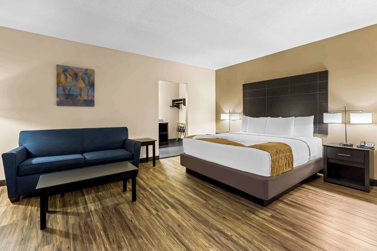 A modern hotel room with a large bed, a sofa, a coffee table, and a painting on the wall.