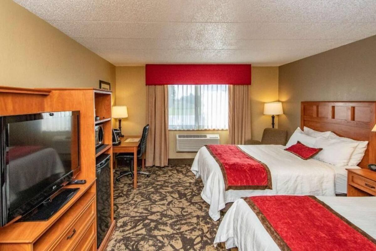 A hotel room with a television, desk, two beds, and a window with curtains.