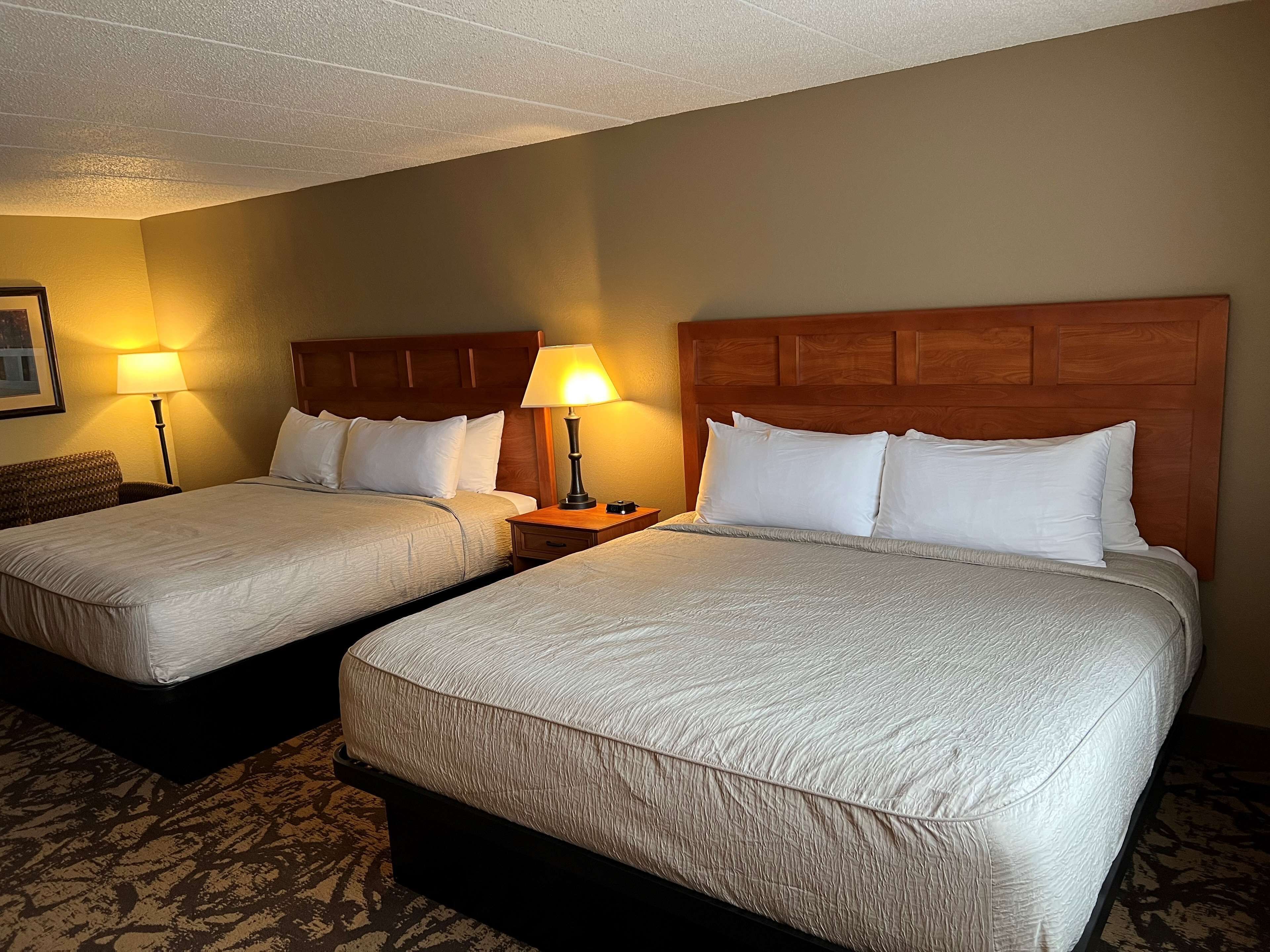 Une chambre d’hôtel avec deux lits, chacun doté d’une tête de lit en bois, de draps blancs et d’une table de chevet avec une lampe.