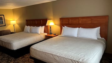 A hotel room with two beds, each with a wooden headboard, white bedding, and a bedside table with a lamp.