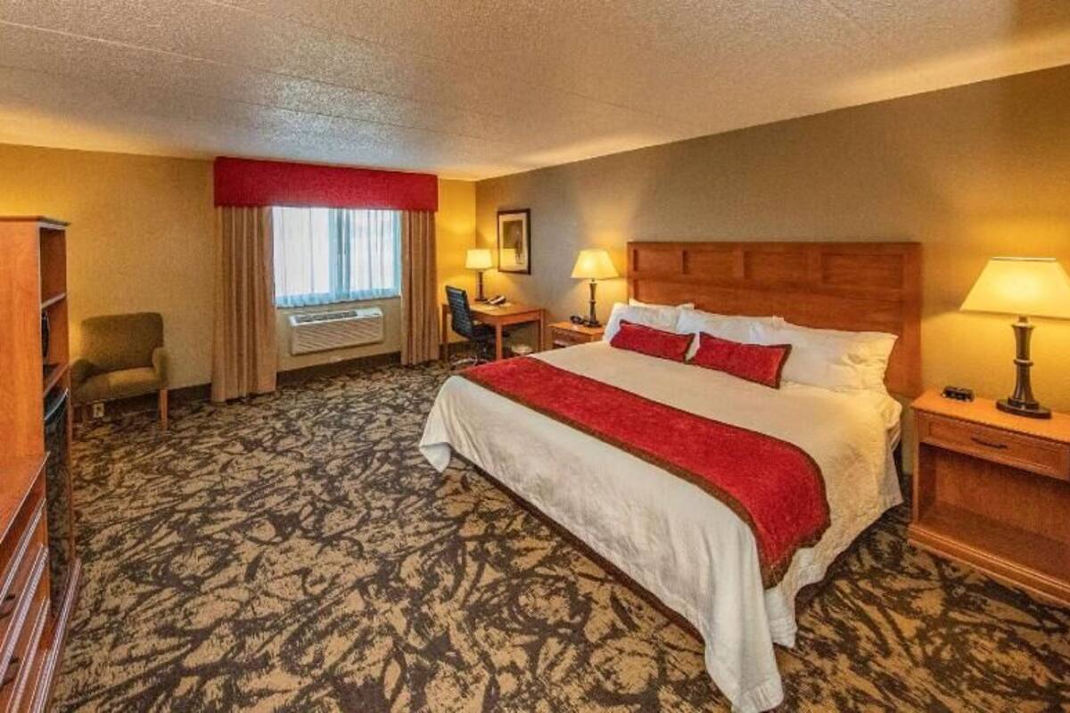 A hotel room with a large bed, a desk, a chair, a television, and a window with curtains.