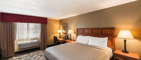 Habitación de hotel con una cama grande, dos mesitas de noche con lámparas, un escritorio con silla, una ventana con cortinas y un calentador fijado a la pared.