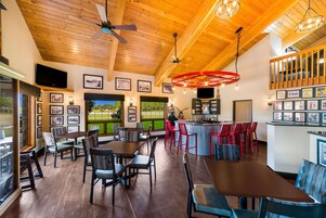 A spacious indoor area with wooden ceilings, multiple tables and chairs, a bar area, and framed pictures on the walls.