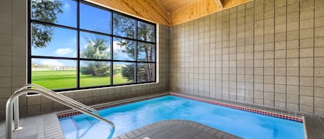 Una piscina interna con vista su un paesaggio verde attraverso ampie finestre.