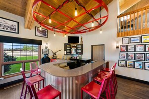 A bar area with a curved counter, red bar stools, a television, and framed pictures on the walls.