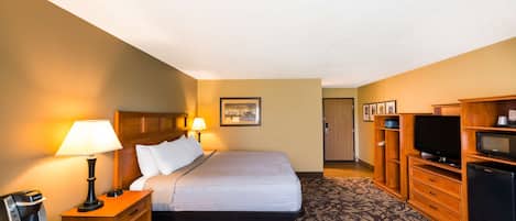 A hotel room with a bed, bedside lamps, a television, a refrigerator, and a wooden cabinet.