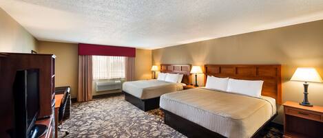 A hotel room with two beds, a TV, a desk, and a carpeted floor.