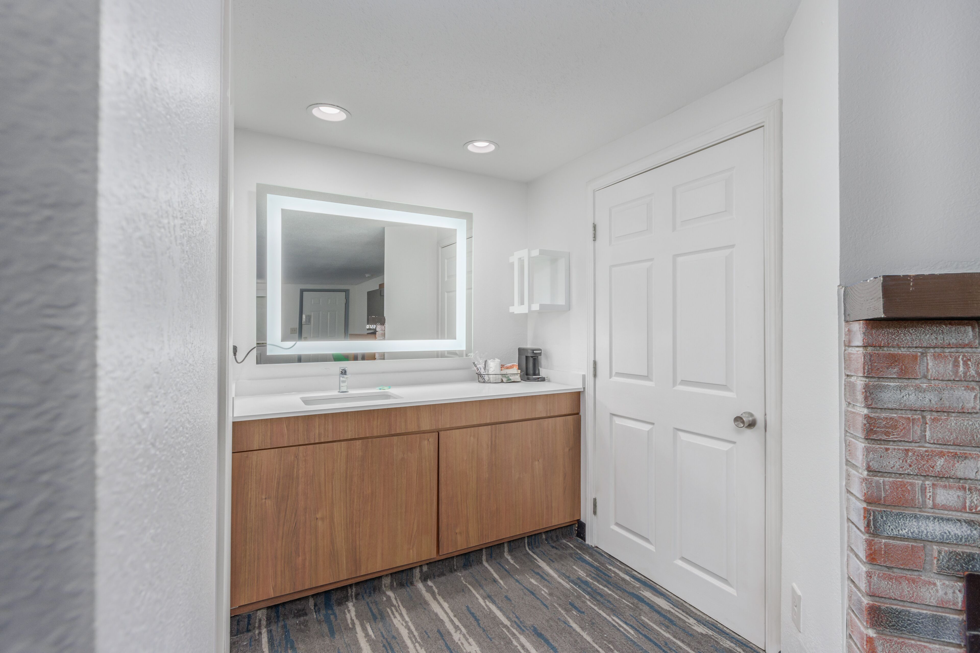 Un baño moderno con tocador de madera, lavabo blanco y un espejo grande.