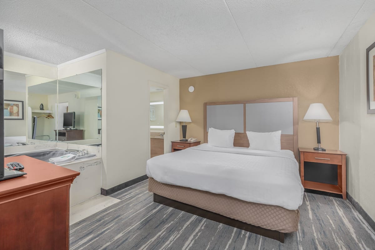 Ein Hotelzimmer mit Bett, Nachttischen, Schreibtisch, Spiegel und einem durch eine geöffnete Tür einsehbaren Badezimmer.