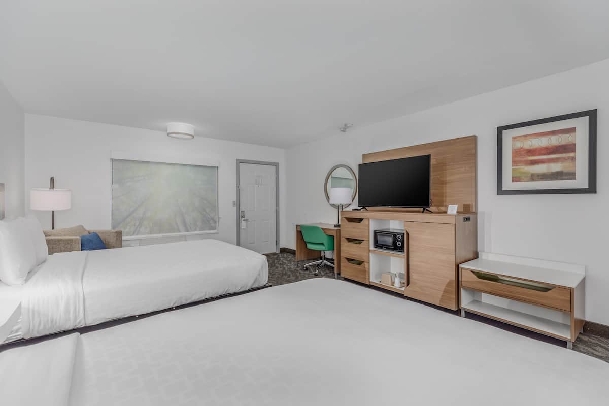 Ein Hotelzimmer mit zwei Betten, einem Schreibtisch, einem Fernseher und einem großen Fenster.