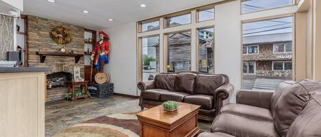 A spacious living room with a fireplace, leather sofas, and large windows offering a view of the street.
