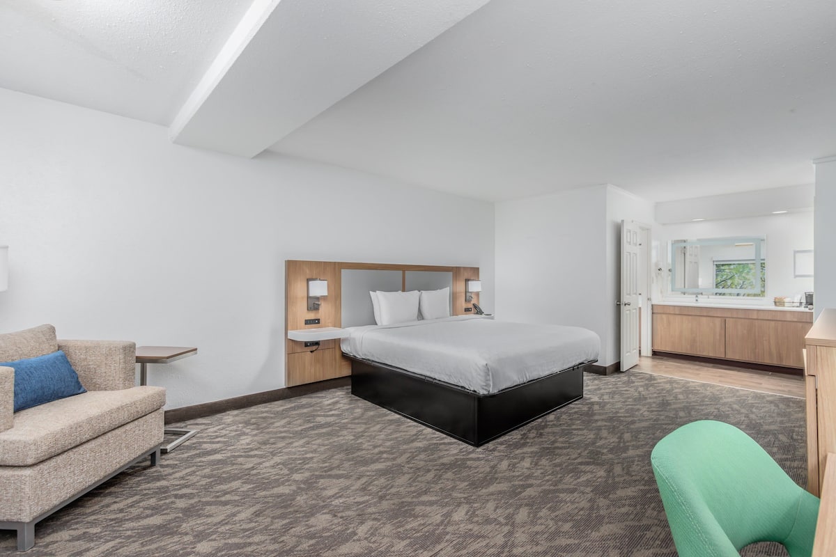 Ein Hotelzimmer mit Bett, Sofa, Sessel, einem kleinen Tisch und einem durchgegangene Tür sichtbaren Badezimmer.