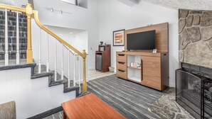 A modern living room with a staircase, a fireplace, and a flat-screen TV mounted on a wooden cabinet.
