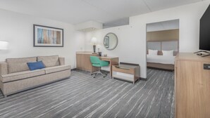A hotel room with a sofa, desk, chair, bed, and a small table.