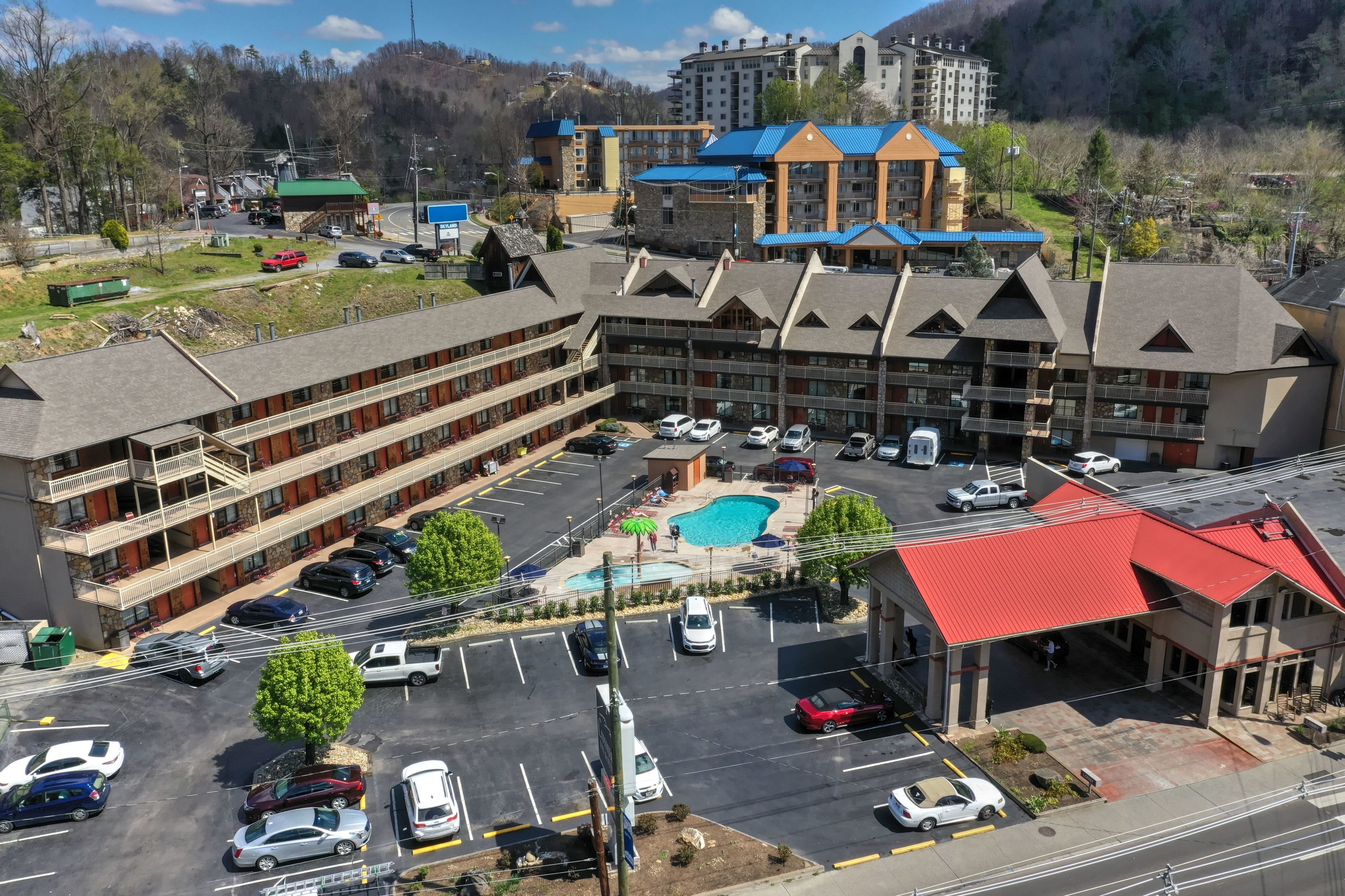 A multi-story hotel with a swimming pool, parking lot, and a view of surrounding buildings.