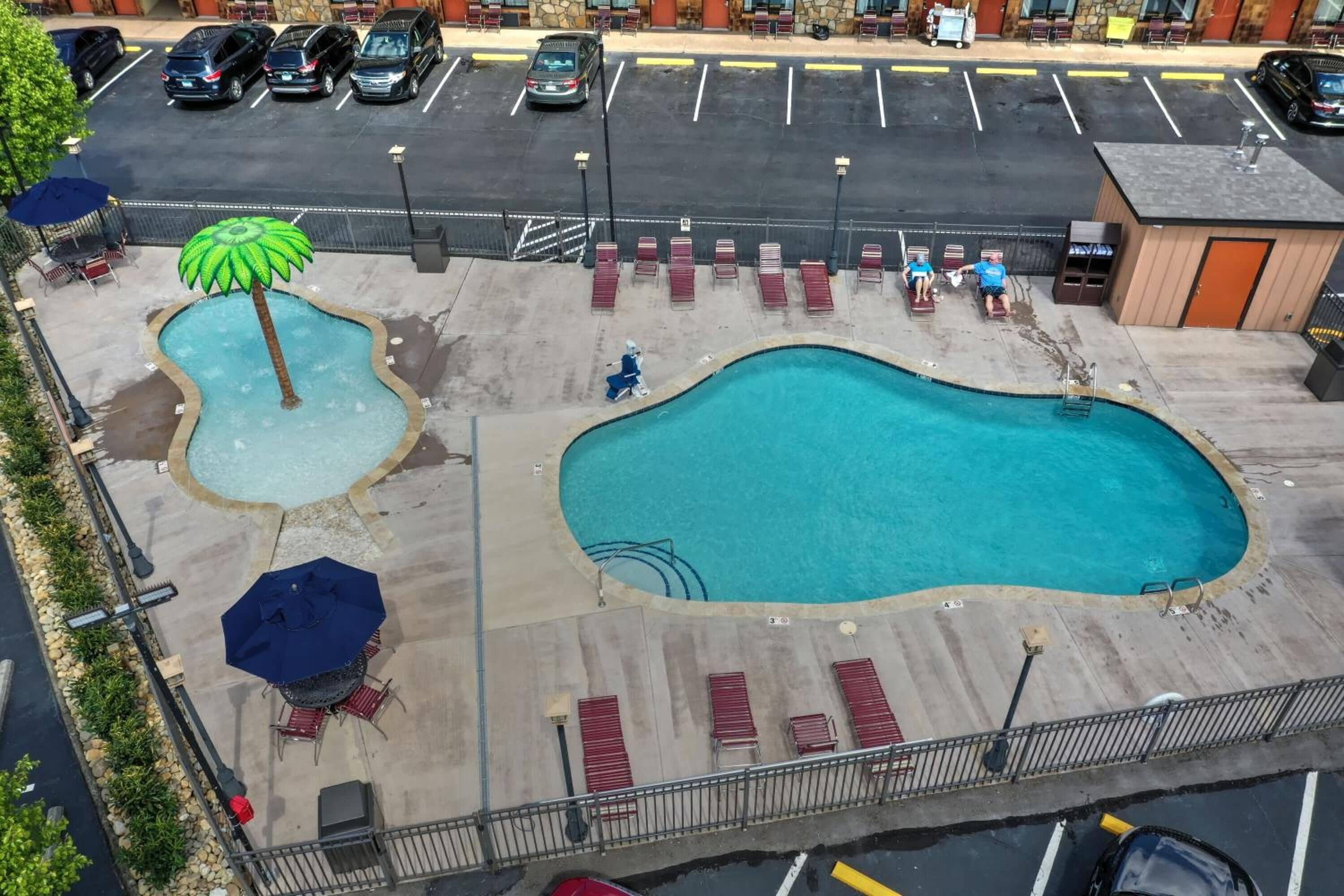 A swimming pool with lounge chairs and umbrellas, surrounded by a parking lot.