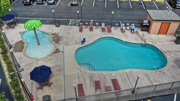 A swimming pool with lounge chairs and umbrellas, surrounded by a parking lot.
