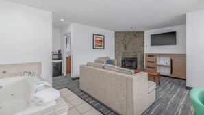 A modern living room with a sofa, a fireplace, a flat-screen TV, and a kitchen area in the background.