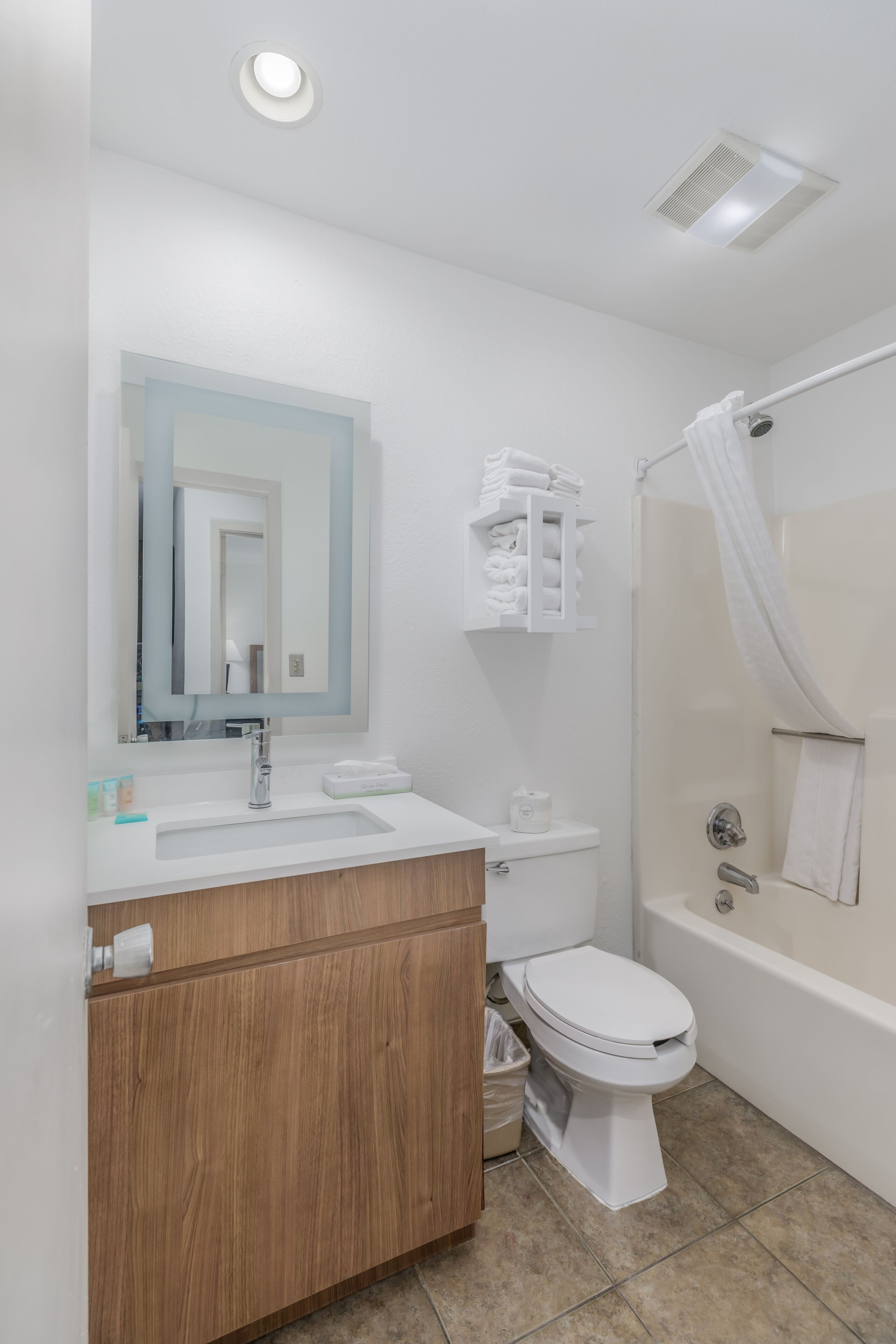 Un baño moderno con tocador de madera, lavamanos blanco, inodoro y bañera con cortina de ducha.