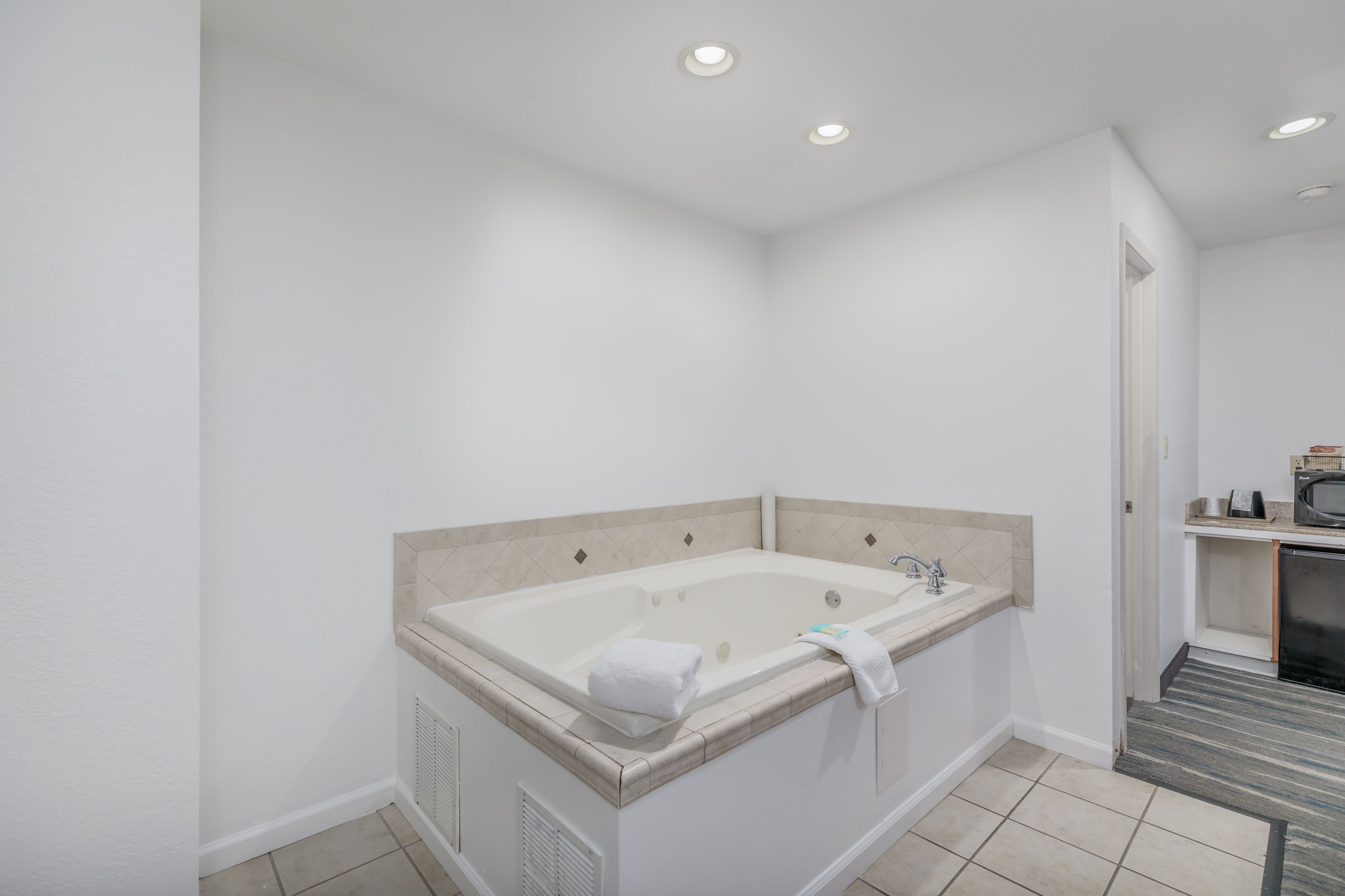 A modern bathroom with a large bathtub, a sink, and a microwave in the corner.