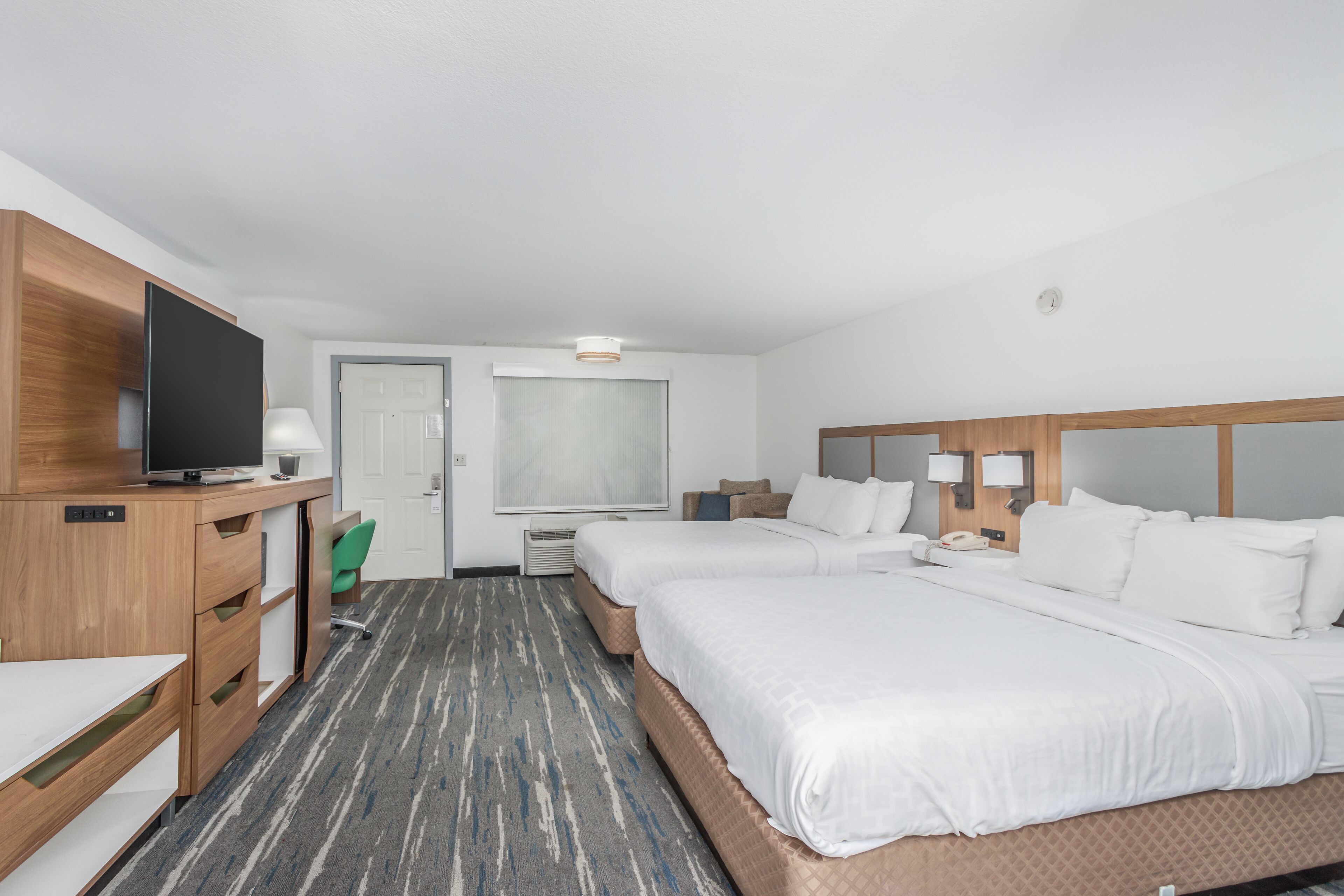A hotel room with two beds, a desk with a television, a chair, and a large window.